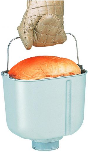a hand in oven glove holding a baked bread in a pan